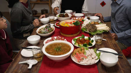 cropped view of senior host of family grandfather clapping hands and gesturing members to sit down at dining table. people pulling out chair, starting to eat big meal for chinese new yearの写真素材