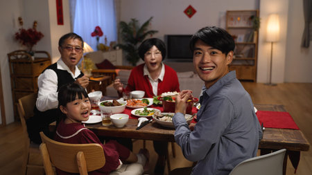 slow motion of happy family at dinner table turning head and look at camera in surprise as someone is serving the main dish for reunion meal at homeの写真素材