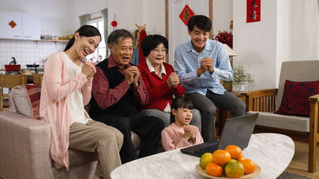 smiling asian big family waving hi and wishing friends a happy chinese new year with congratulation hand gestures through video chat on computer in the living roomの写真素材