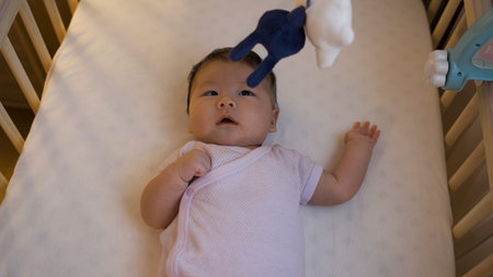 high angle view portrait of innocent newborn infant is staring at the hanging toy in the baby bed...