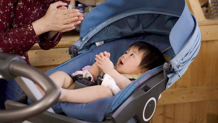 cropped shot innocent Korean baby lying in the stroller at home is looking at her mom who is...
