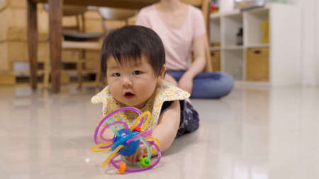 selective focus energetic cute toddler holding and playing with a colorful toy on the home floor and lifting her body while slowly moving ahead.の写真素材