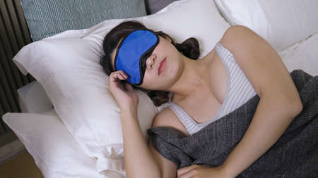 portrait woman wearing eye cover turning and tossing in bed in the early morning. real moments. health and wellness concept.の写真素材