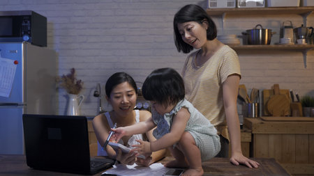 adorable asian toddler squatting on the dining table is using pen to tap hard while her lesbian...