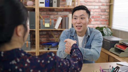 asian male startup owner is looking at the female investor in surprise while bowing and carrying her hands with appreciation in the office.の写真素材