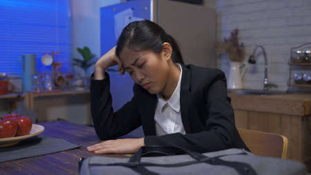 frustrated female worker holding her head and hand tapping on table is worrying about her poor performance after work in the home dining room at nightの写真素材