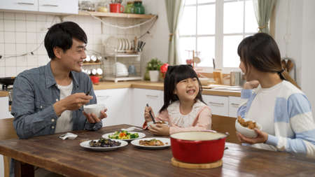 beautiful Asian family of three eating together in a modern dining room with daylight. caring father filling wifeâs bowl with meat as the mother also fills daughterâs bowl with foodの写真素材