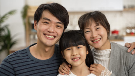 headshot portrait of beautiful asian family of three embracing each other and looking at camera with...