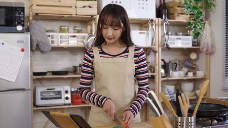 portrait happy female beginner using a tablet computer to learn cutting vegetables from online video at home kitchen. technology and genuine lifestyle.の写真素材