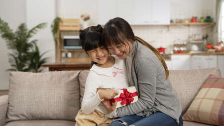 surprised asian mother embracing hug daughter for getting motherâs day gift at home. the girl showing present from behind as her mom is covering eyesの写真素材