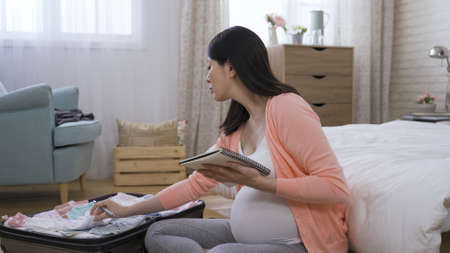 expectant mother is making sure she has got all the accessories for her baby and writing in a notebook at background bright home interior.の写真素材