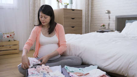 expectant mother sitting on the bedroom floor is folding baby clothes with concentration in the morning at home.の写真素材