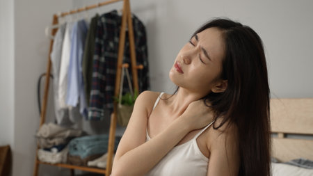 shoulder shot of a Korean girl exercising her stiff neck muscles and massaging her painful shoulders after getting up in the morning in the bedroom at home.の写真素材