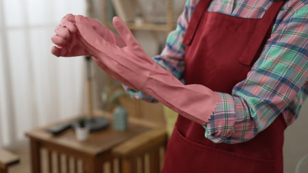close up of woman wearing protective rubber gloves before doing housework. focus view on female maid hands putting on pink hand protection while ready for cleaning in house. household chores conceptの写真素材