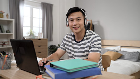 portrait of a cheerful asian college student turning head to smile at the camera while learning from...