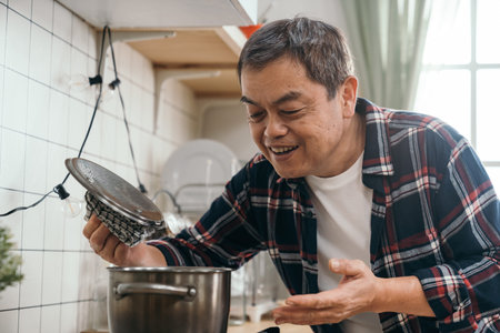 retired Asian man's eyes sparkle as he lifts the lid of the soup pot, enjoying the delicious...