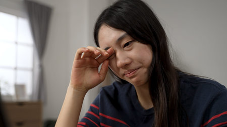 closeup view of an Asian young woman suffering eye irritation is rubbing while learning from home at...