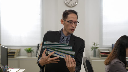 closeup shot of asian male manager carrying and putting heavy paperwork on his workerâ€™s desk....