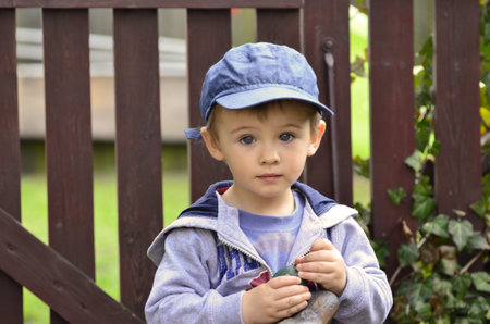The picture shows a little boy who stood in play against the fence in garden 