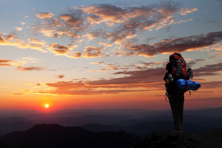 Evening silhouette - view of man on mountains with big rucksack on backの写真素材