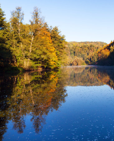 Ohre river and autumnal view of forest mirroring on water surface lake