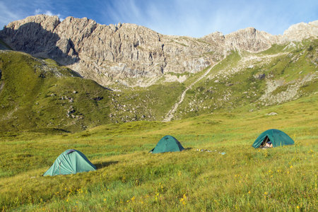 three tents on a meadow in the mountains under a rock wallの写真素材