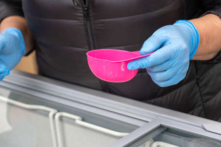 ice cream vendor with blue rubber gloves serves ice cream in a small pink dish.の写真素材
