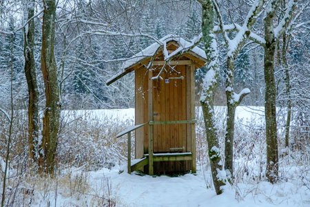 Outdoor wooden toilet house covered with snow on winter forest and trees background. Among the trees by the tourist trailの写真素材