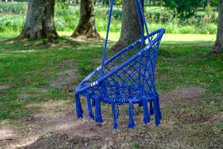 Comfortable hanging wicker blue chair in the summer garden. A cozy hygge place for a weekend in the...
