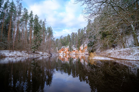 The river Salaca is meandered by high sandstone cliffs. Skanaiskalns nature park. November is the first snow in Mazsalaca in Latviaの写真素材