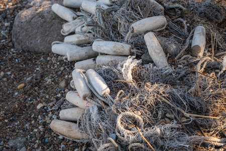 Discarded fishing net and plastic bottles polluting a rocky beach.の写真素材
