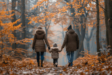 A family holding hands and walking through an autumn forest with colorful leaves, creating a warm and loving scene.の素材