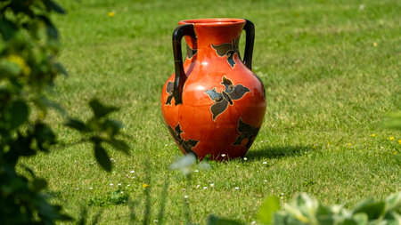 A vibrant terracotta vase with black floral patterns placed on a grassy lawn, adding a decorative touch to the garden.の写真素材