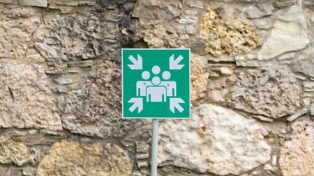 Green assembly point sign indicating a safe gathering area, mounted against a textured stone wall for emergency situations.の写真素材