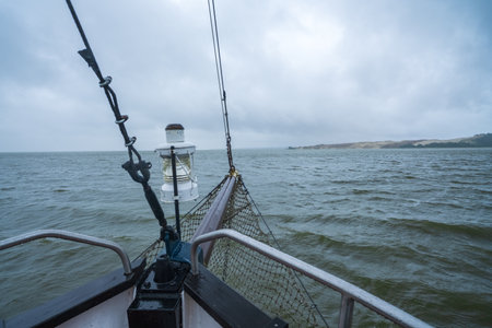 View from a boat sailing on the water under a cloudy sky, with a distant shoreline visible on the horizon.の写真素材