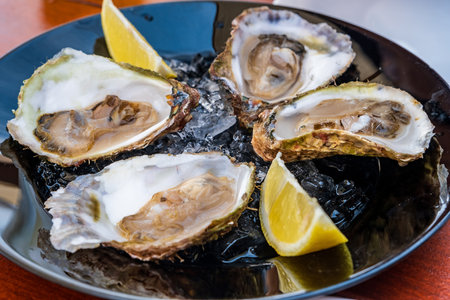 A plate of fresh oysters served on ice with lemon wedges, ready to eat, highlighting the freshness and deliciousness of this seafood delicacy.の写真素材