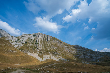 A striking rocky mountain ridge with unique vertical formations, set against a bright blue sky with scattered clouds.の写真素材