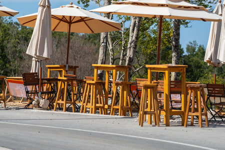 An outdoor cafe features wooden tables and chairs under large beige umbrellas, creating a cozy, sunlit dining atmosphere.の写真素材