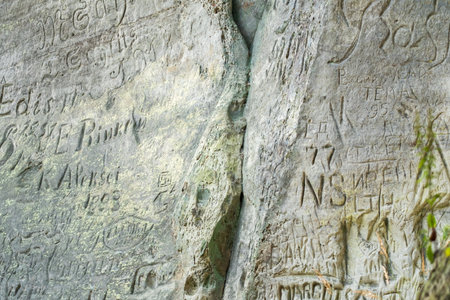 Close-up of various carvings and graffiti etched into a weathered rock face, showcasing historic and personal inscriptions.の写真素材
