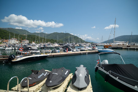 A sunny marina with a variety of boats and jet skis docked in calm waters, surrounded by scenic mountains.の写真素材