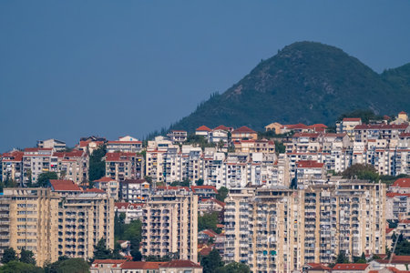 A dense cluster of residential apartment buildings with red-tiled roofs, located in a coastal city with a backdrop of green hills.の写真素材