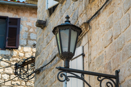 A black vintage lantern mounted on a stone wall, surrounded by rustic windows and wiring, capturing the charm of a historic street setting.の写真素材