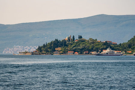 A scenic coastal village with a ferry passing near an island, featuring a historic church surrounded...