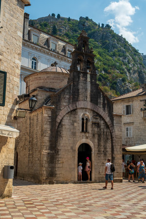 Tourists explore a small historic stone church with a bell tower located in a picturesque Mediterranean town square.の写真素材