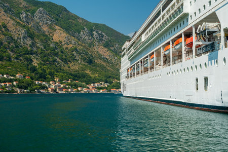 A close-up view of a cruise ship docked near a coastal village with mountainous landscapes and clear blue waters.の写真素材