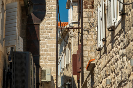 A narrow alleyway framed by old stone buildings with shutters and air conditioning units, showing a blend of historic and modern elements.の写真素材