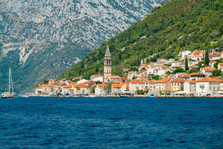 A charming coastal village with red-tiled rooftops and a prominent bell tower, nestled between the...