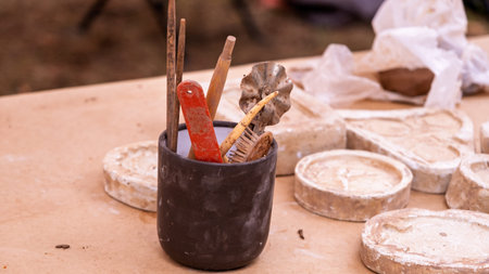 Close-up of various sculpting tools in a container alongside clay molds on a wooden workbench in a...
