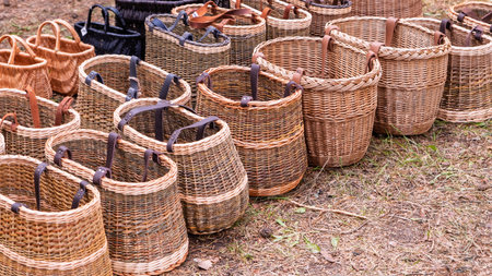 A row of handcrafted willow baskets in various shapes and sizes, featuring sturdy leather straps,...