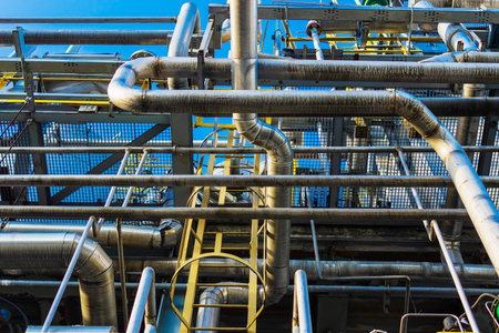 A bunch of metal pipes stand at a gas processing plant against the blue sky.